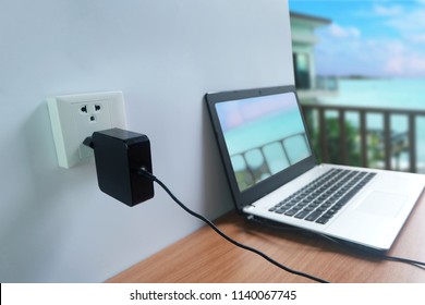 Plug In Power Outlet Adapter Cord Charger On A White Wall Of The Laptop Computer On Wooden Floor