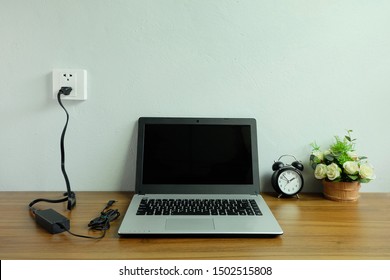 Plug In Power Outlet Adapter Cord Charger On A White Wall Of The Laptop Computer On Wooden Floor