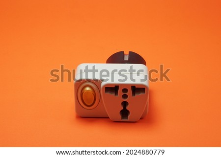 Plug socket converter from UK or US standard plug to Indonesian standard. Plug socket converter with switch on isolated orange background.