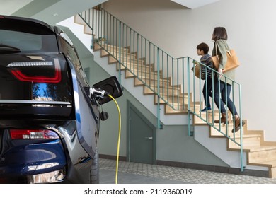 Plugged cable charging an electric family car in a particular garage. - Shutterstock ID 2119360019