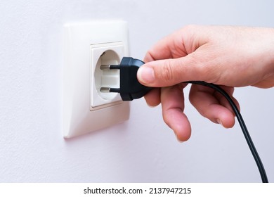 Plugging a black electrical plug with a woman's hand into a white plastic socket on a wall.