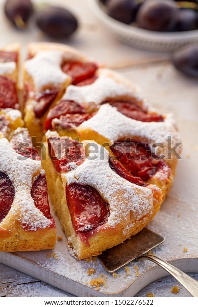 Plum cake, traditional homemade  cake\
with fruit divided into parts, sprinkled with powdered sugar on a\
white board, close-up view. Fruit cake,\
dessert