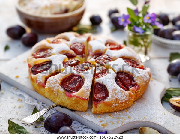 Plum cake, traditional homemade  cake\
with fruit, divided into portions, sprinkled with powdered sugar on\
a white board, close-up view. Fruit cake,\
dessert
