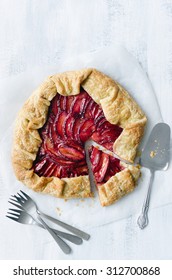 Plum Galette On Baking Wax Paper Shot From Overhead, Whole With One Serving Slice Cut Out