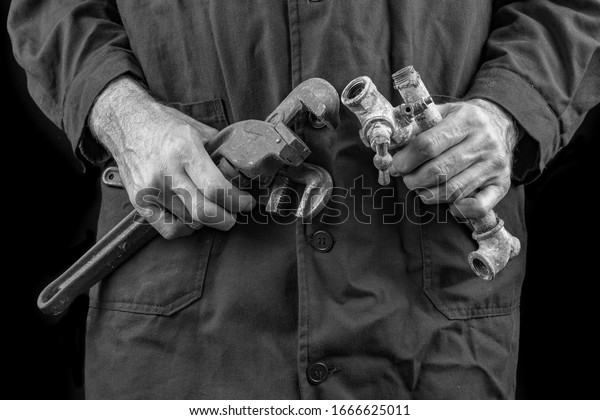 Plumber in an apron
holding a wrench and old pipes. Accessories and parts for builders.
Dark background.