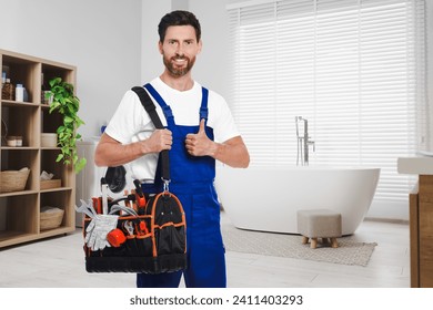 Plumber with bag of instruments showing thumbs up in bathroom, space for text