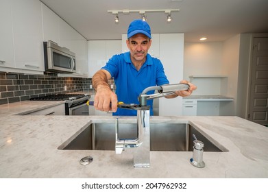 Plumber In Blue Uniform Using Pliers To Repair Or Install A Kitchen Faucet