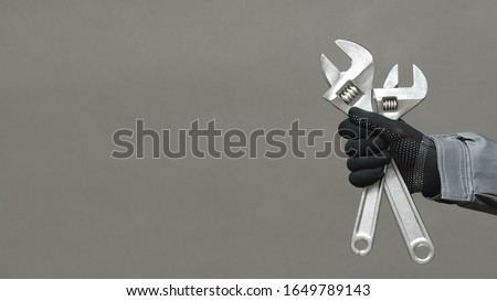Plumber or car mechanic business card template. Worker holding in hands adjustable wrench close up over gray background with copy space.