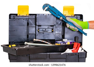 Plumber Or Carpenter Tool Box Isolated. Black Plastic Tool Kit Box With Assorted Tools And A Mans Hand With A Glove Holds A Big Pipe Wrench. Isolated On A White Background.