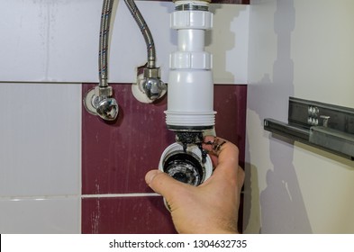 Plumber cleans sewer drain in siphon under sink