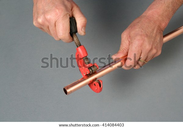 Plumber cutting\
a copper pipe with a pipe\
cutter.