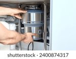A plumber with gloved hands installs a household waste shredder for the kitchen sink. A technician installs or repairs a household waste shredder in the kitchen.