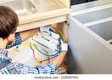 Plumber hand in gloves replace water filter cartridges at kitchen. Fix purification osmosis system. Technician installing or repairing system of water filtration. - Powered by Shutterstock