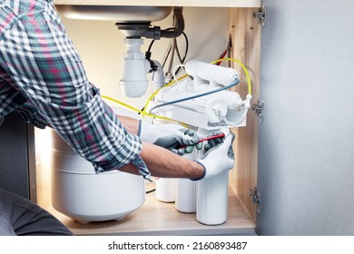 Plumber hand in gloves replace water filter cartridges at kitchen. Fix purification osmosis system. Technician installing or repairing system of water filtration. - Powered by Shutterstock