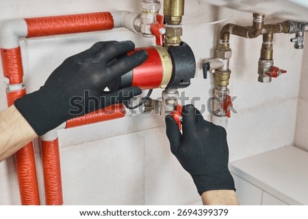 Plumber hands installing circulation pump for a heating system, connecting pipes and control valves