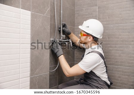 Plumber installing water taps shower stall, work in bathroom.