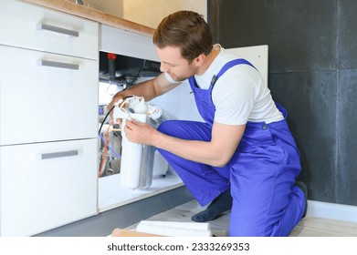 Plumber installs or change water filter. Replacement aqua filter. Repairman installing water filter cartridges in a kitchen. Installation of reverse osmosis water purification system - Powered by Shutterstock