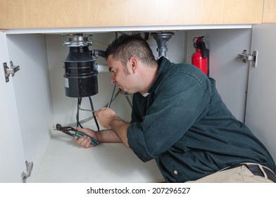 A Plumber Laying Under A House Hold Sink Working On A Garbage Disposal.