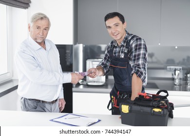 A Plumber Man Communicates With A Client Who Pays For The Work Done. The Old Man Gives The Plumber A Fee. A Black Box For Tools Is Next To It.