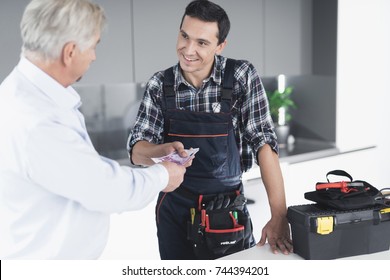 A Plumber Man Communicates With A Client Who Pays For The Work Done. The Old Man Gives The Plumber A Fee. A Black Box For Tools Is Next To It.