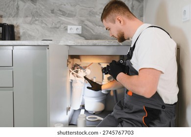 Plumber performing maintenance on a complex under sink water filtration system, ensuring clean drinking water in a modern kitchen