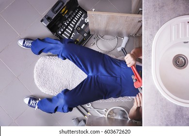 Plumber Repairing Sink Pipes In Kitchen