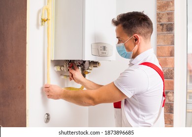 The Plumber Repairs A Boiler In A Medical Mask