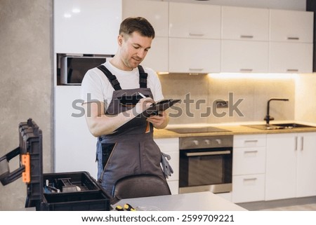 Plumber taking notes on a clipboard while inspecting a kitchen, ensuring efficient plumbing services and maintenance