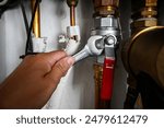 Plumber is tightening a nut on a water heater pipe using an adjustable wrench.