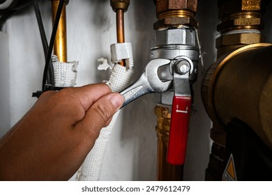 Plumber is tightening a nut on a water heater pipe using an adjustable wrench.