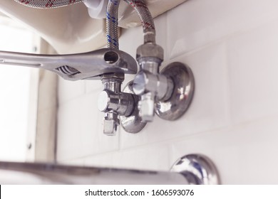 Plumber Turns Nut On Angle Valve Under Wash Basin Using Spreading Wrench.