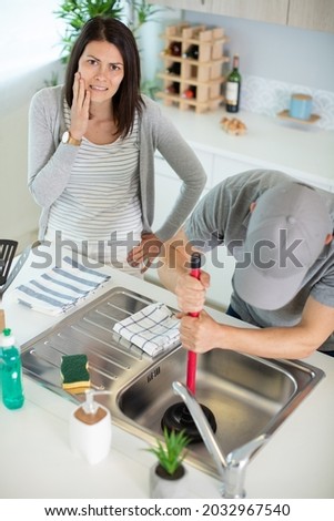 plumber unblocking a sink while worried woman watches