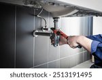 Plumber uses wrench to repair water pipe under sink There is maintenance to fix the water leak in the bathroom.with red wrench, plumbing install concept.