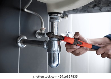 Plumber uses wrench to repair water pipe under sink There is maintenance to fix the water leak in the bathroom.with red wrench, plumbing install concept. - Powered by Shutterstock