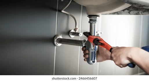 Plumber uses wrench to repair water pipe under sink There is maintenance to fix the water leak in the bathroom.with red wrench, plumbing install concept. - Powered by Shutterstock