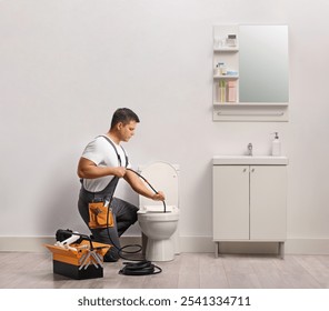 Plumber using a drain snake for clogged toilet in a bathroom