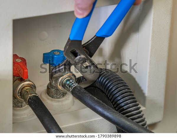 Plumber using a wrench to\
attach water supply line to the shut-off valve for clothes washing\
machine.