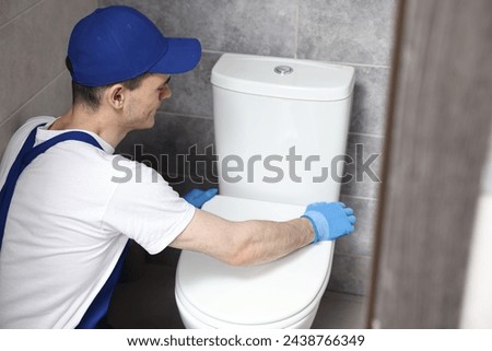 Plumber wearing protective gloves repairing toilet bowl in water closet