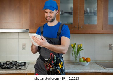 Plumber Wearing A Tool Belt With Various Tools Using Tablet During Work In Kitchen