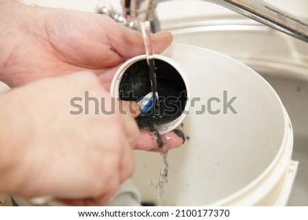 Plumber worker hands cleans clogged plastic water trap siphon cap under water jet with brush, plumbing maintenance
