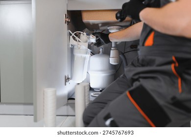 Plumber working on installing or maintaining a reverse osmosis water filtration system and pipes under a modern kitchen sink