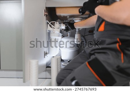 Plumber working on installing or maintaining a reverse osmosis water filtration system and pipes under a modern kitchen sink