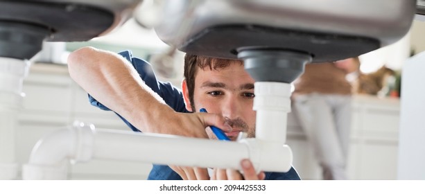 Plumber Working On Pipes Under Sink