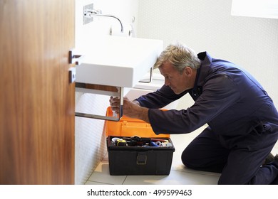 Plumber Working On Sink In Bathroom