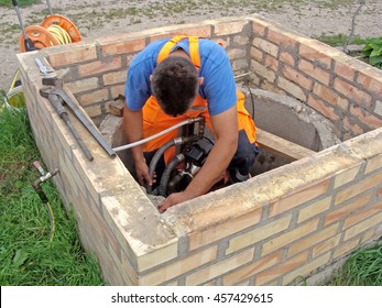 Plumber Is Working In Opened Well Repairing Water Pump.