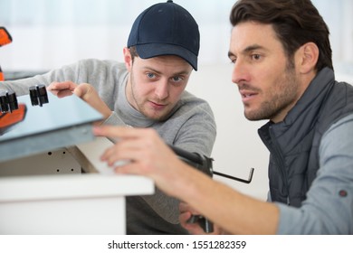 Plumber With Young Trainee Repairing Cooker