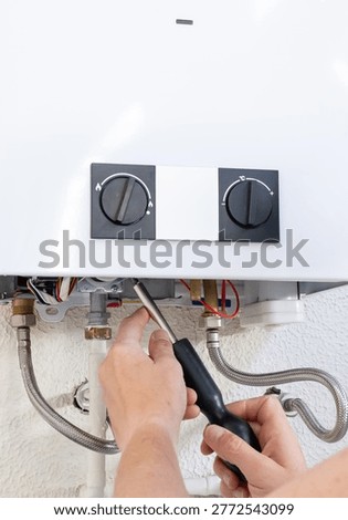 Plumber's hands using a screwdriver to install or repair a gas water heater boiler, close-up of professional maintenance work on residential heating system and piping