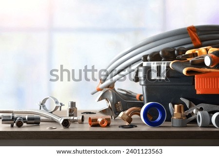 Plumber's toolbox with material around on wooden table with window in background. Front view. Horizontal composition.