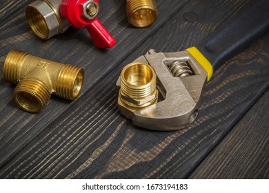 Plumbing brass fittings and adjustable spanner closeup on a black wooden boards during repair or replacement of spare parts