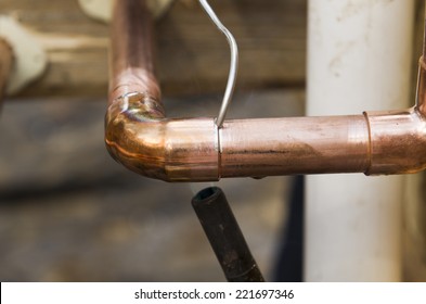 Plumbing contractor works sweating the joints on the copper pipe domestic water system on a luxury custom home